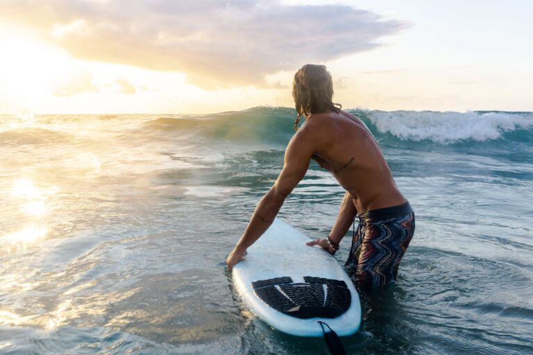 Man knee deep in the ocean holding his surfboard getting ready to surf.